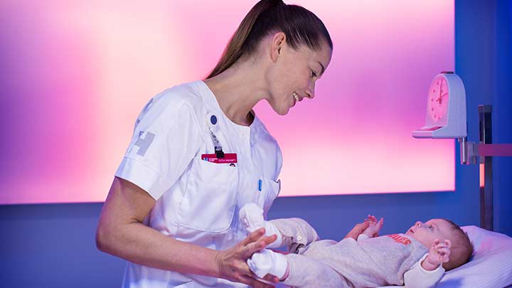 ممرضة تقيس وزن طفلاً رضيعًا في غرفة ذات إضاءة خافتة - إضاءة منشآت الرعاية الصحية
